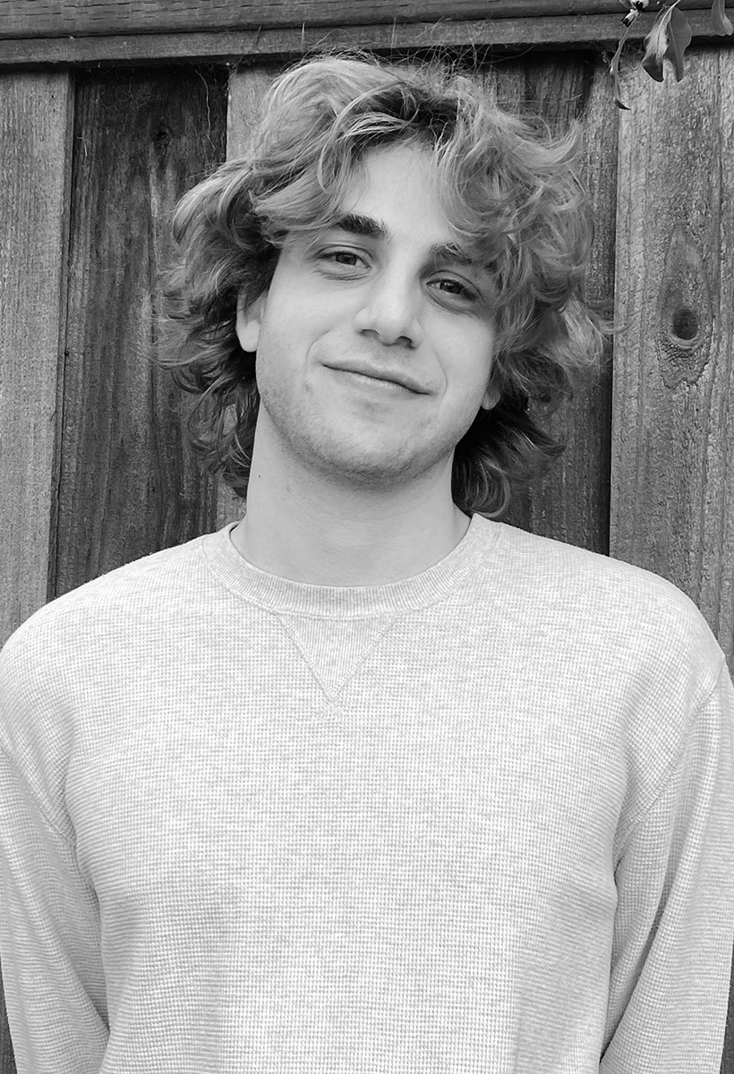 griffin is a young man with wavy longish hair, wearing a waffle shirt and standing against a wooden fence