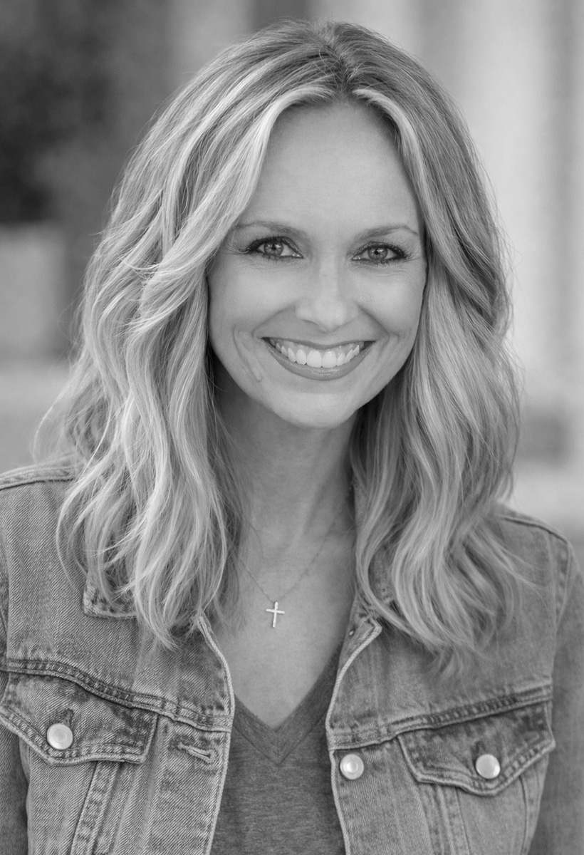 leigh green is a woman with shoulder length blonde hair. she is wearing a jean jacket, v-neck short, and a cross.