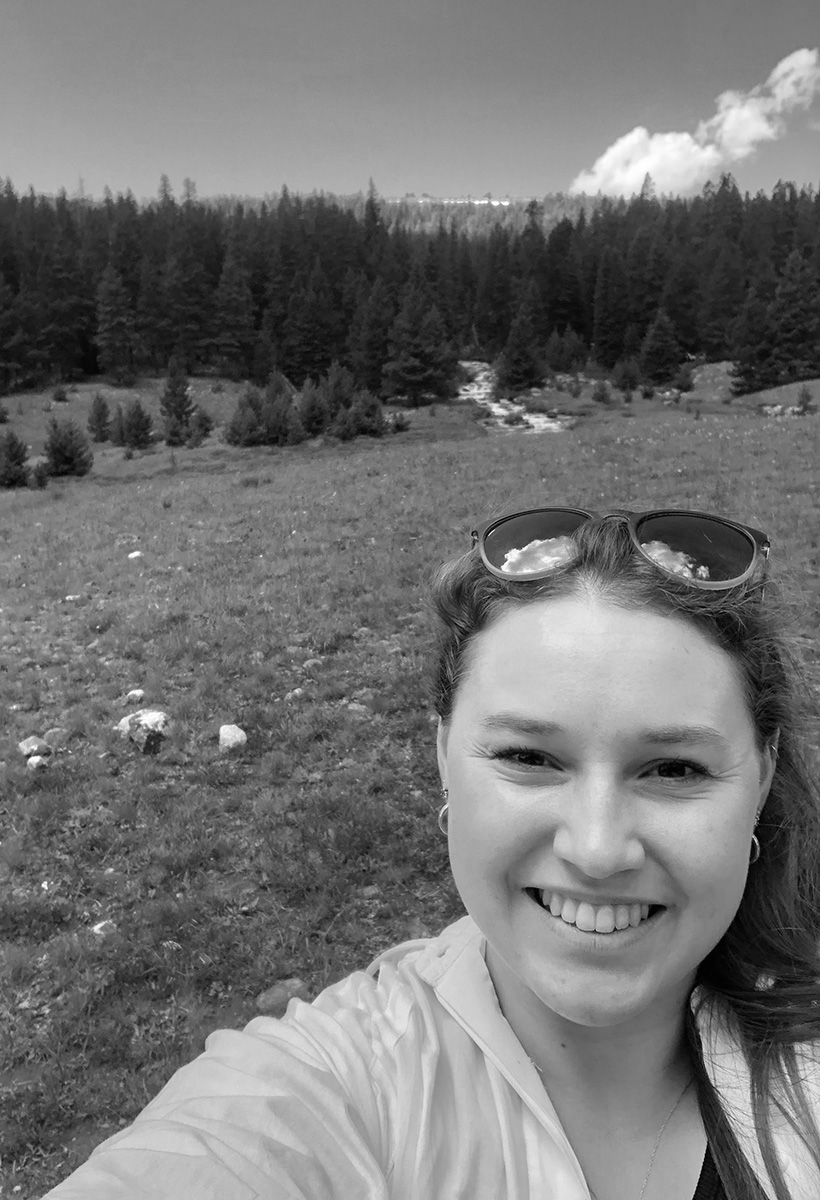 micahela is a young woman taking a selfie in a wilderness area. she has long brown hair and is wearing her sunglasses on top of her head