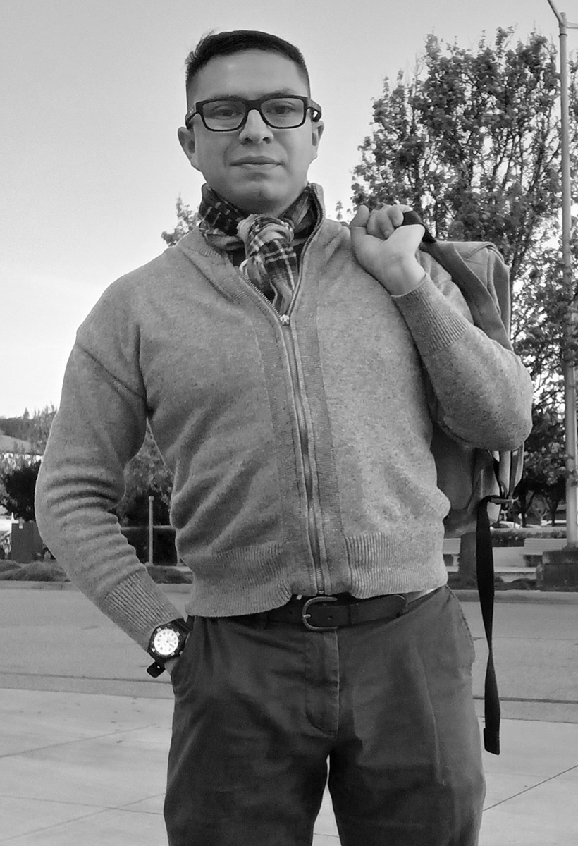 vicente is a youngish man wearing a sweater, plaid scarf and chinos. he has short brown hair and wears glasses with black plastic rims